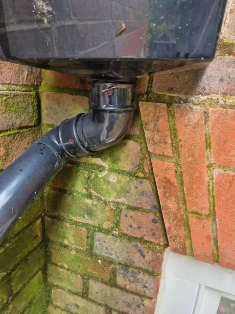 Downpipe and hopper head on a brick wall being checked for blockages
