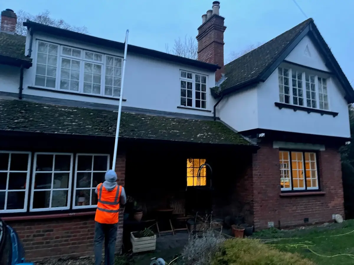 Gutter cleaner clearing the gutters of a period house at dusk using a pole system