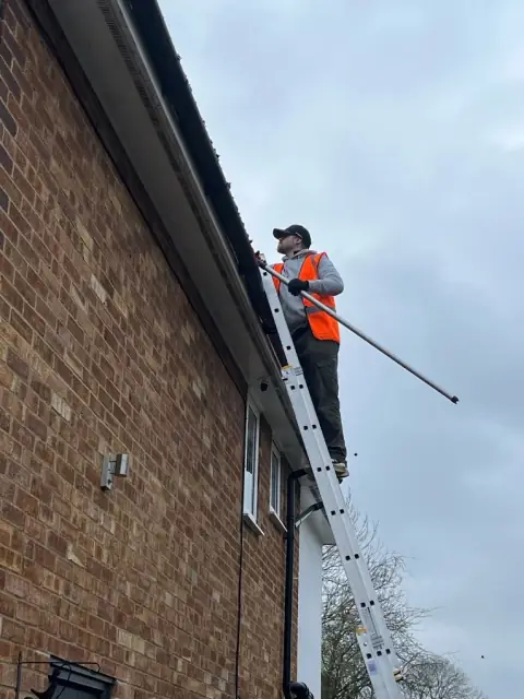 Gutter cleaner in a hi-vis vest clearing a gutter from a ladder