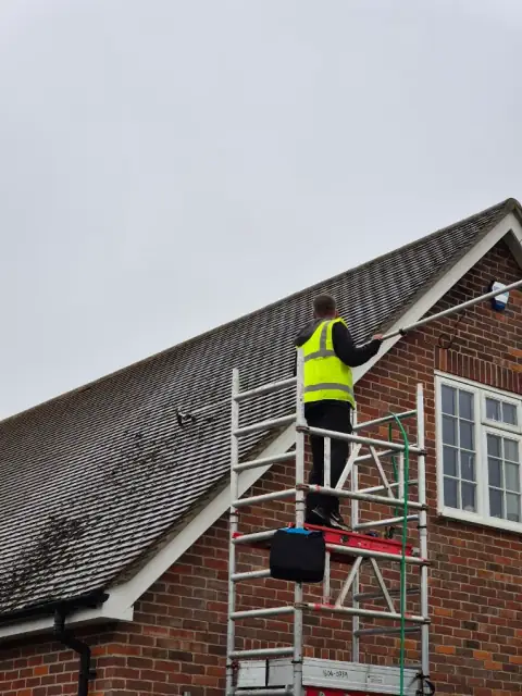 Roof cleaner scraping moss from a tiled roof from a scaffold tower