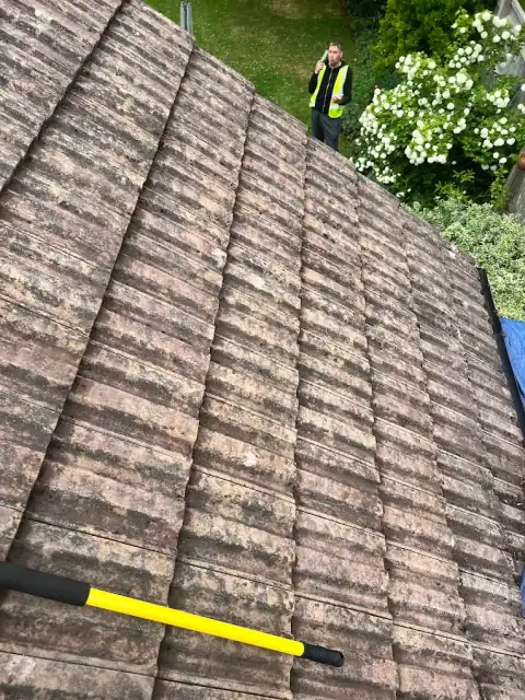 Cleaned clay pantile roof photographed from the ridge with a scraping tool resting on the tiles